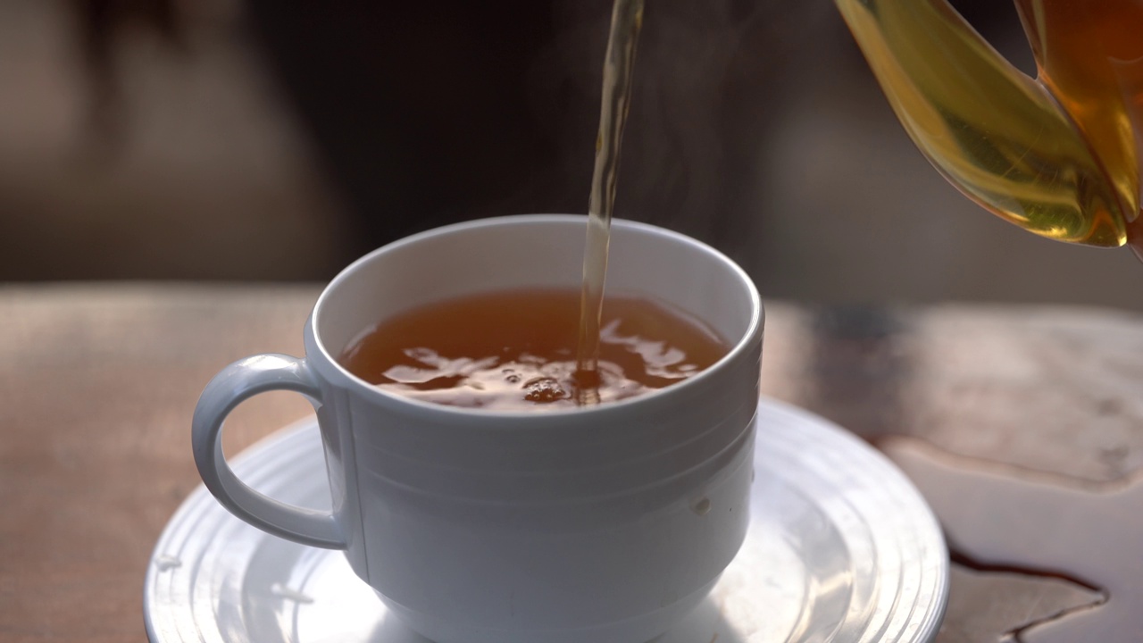 将茶从透明玻璃茶壶中倒入陶瓷茶杯中。健康饮料的概念。视频素材