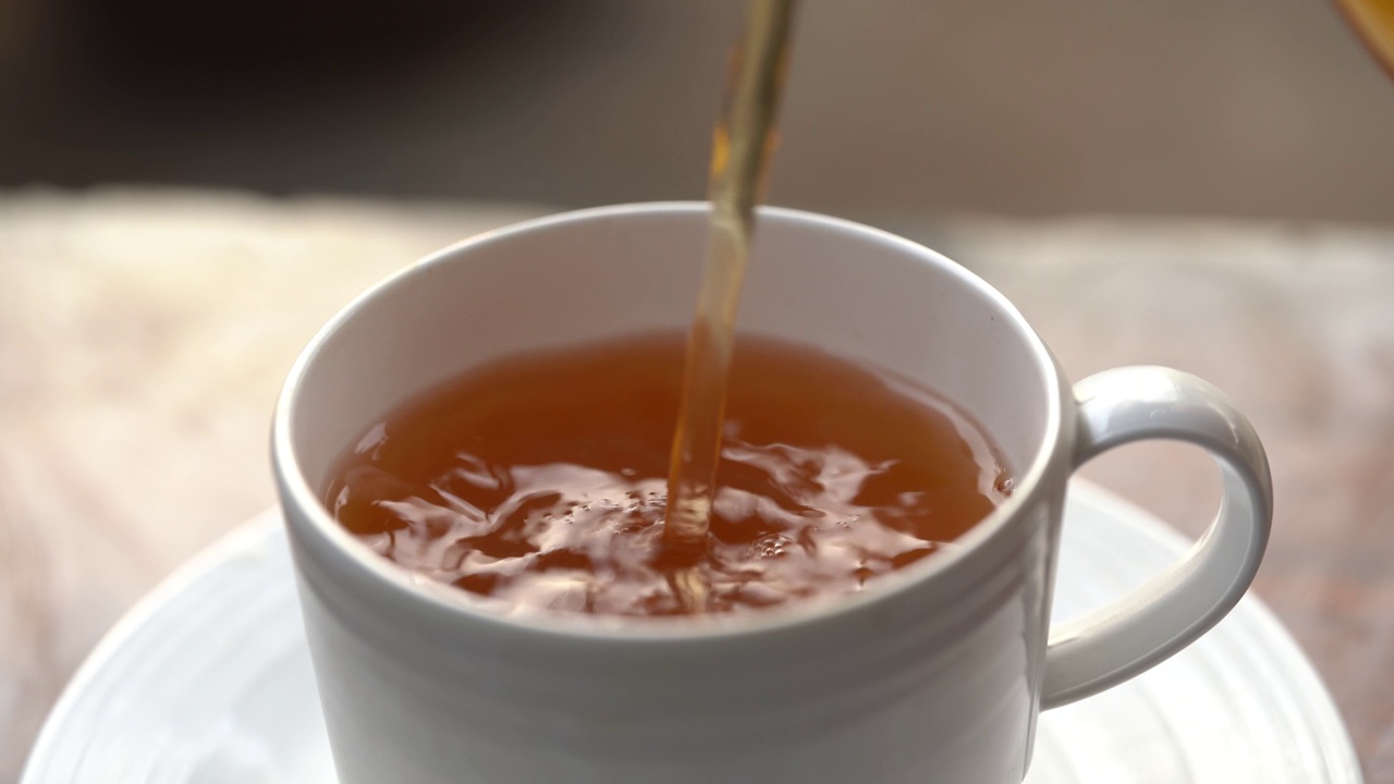 将茶从透明玻璃茶壶中倒入陶瓷茶杯中。健康饮料的概念。视频素材