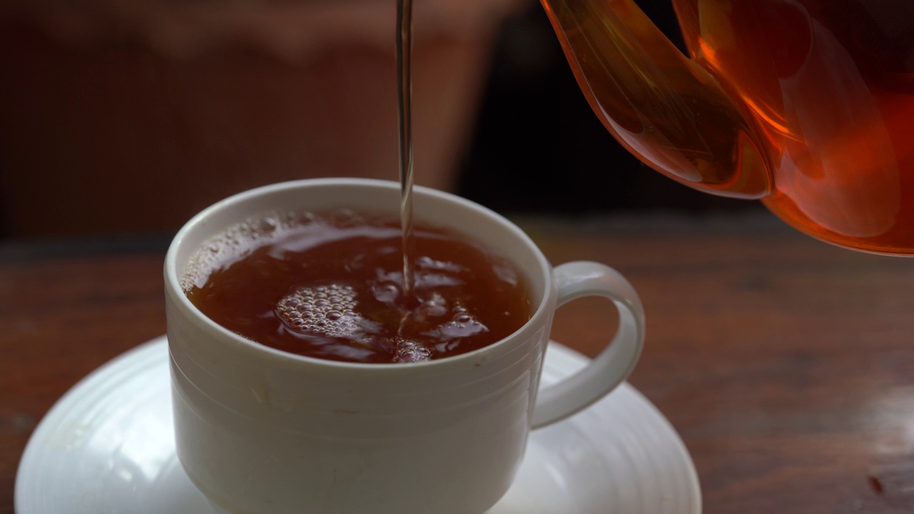 将茶从透明玻璃茶壶中倒入陶瓷茶杯中。健康饮料的概念。视频素材