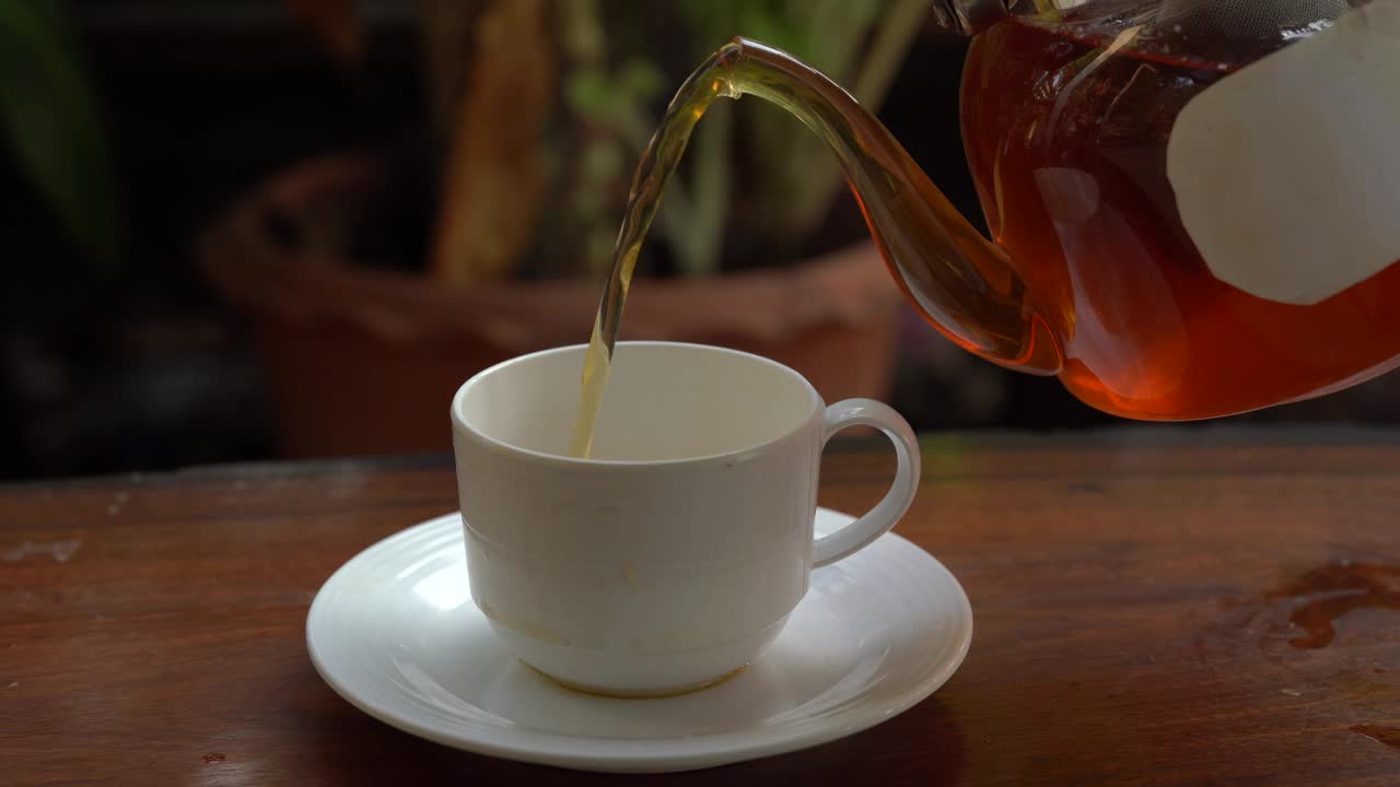 将茶从透明玻璃茶壶中倒入陶瓷茶杯中。健康饮料的概念。视频素材