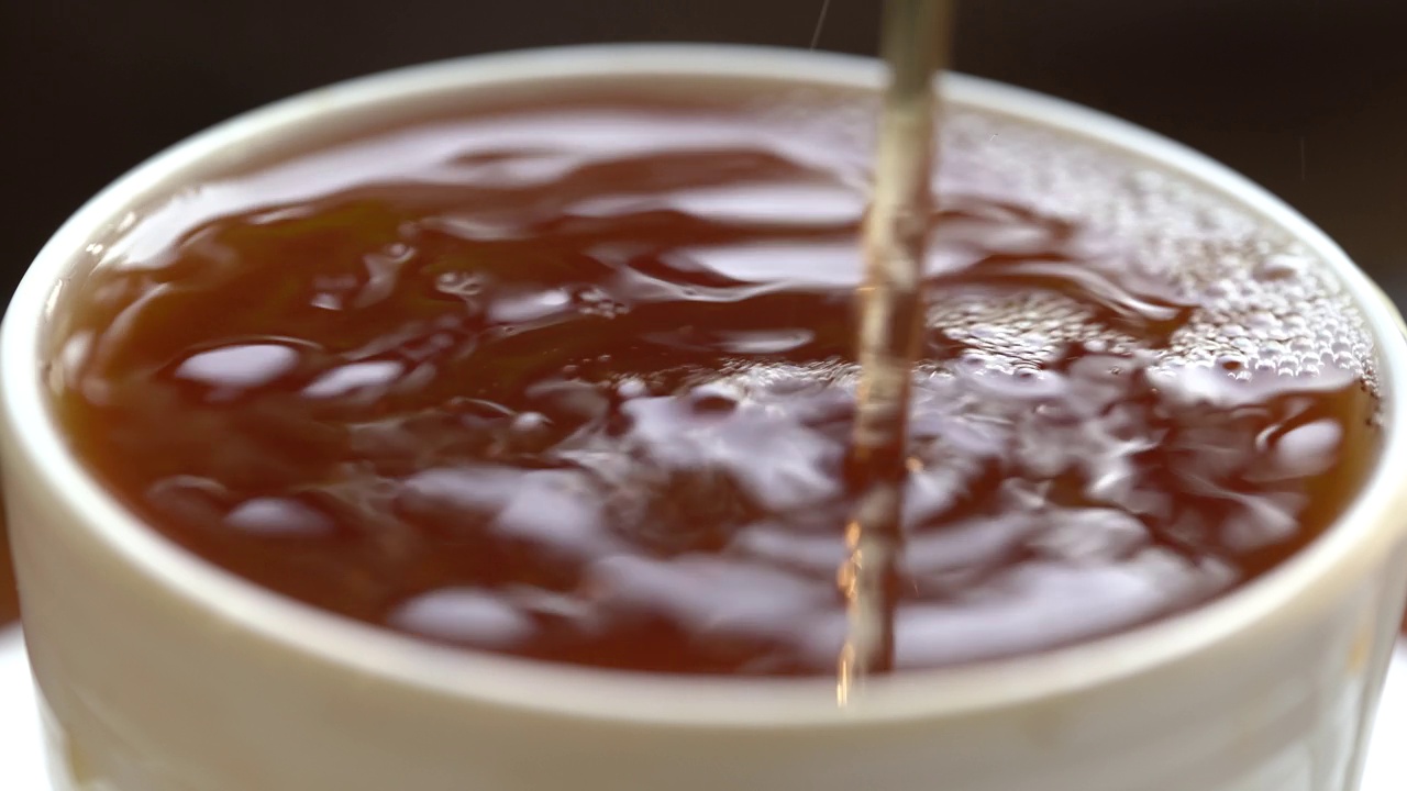 将茶从透明玻璃茶壶中倒入陶瓷茶杯中。健康饮料的概念。视频素材