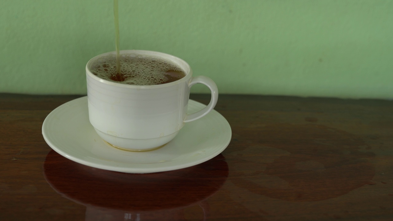 将茶从透明玻璃茶壶中倒入陶瓷茶杯中。健康饮料的概念。视频素材