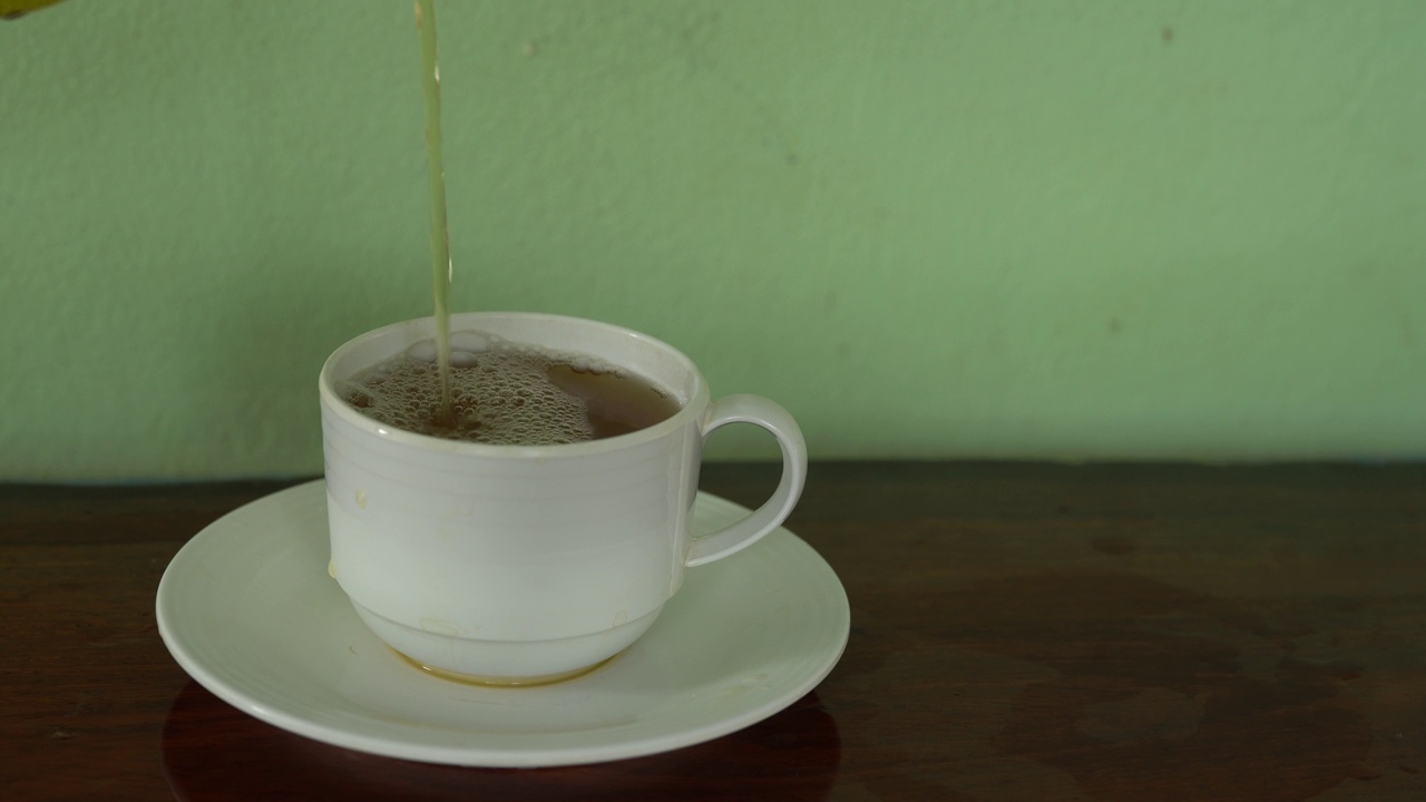 将茶从透明玻璃茶壶中倒入陶瓷茶杯中。健康饮料的概念。视频素材