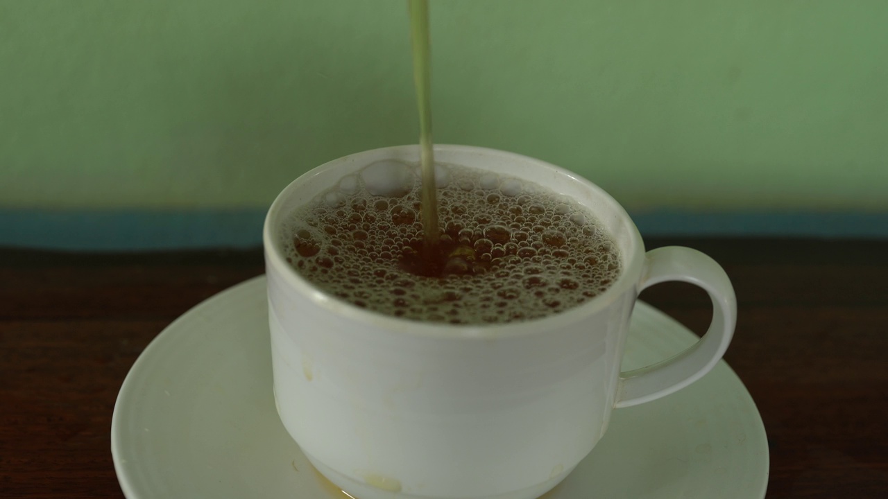 将茶从透明玻璃茶壶中倒入陶瓷茶杯中。健康饮料的概念。视频素材