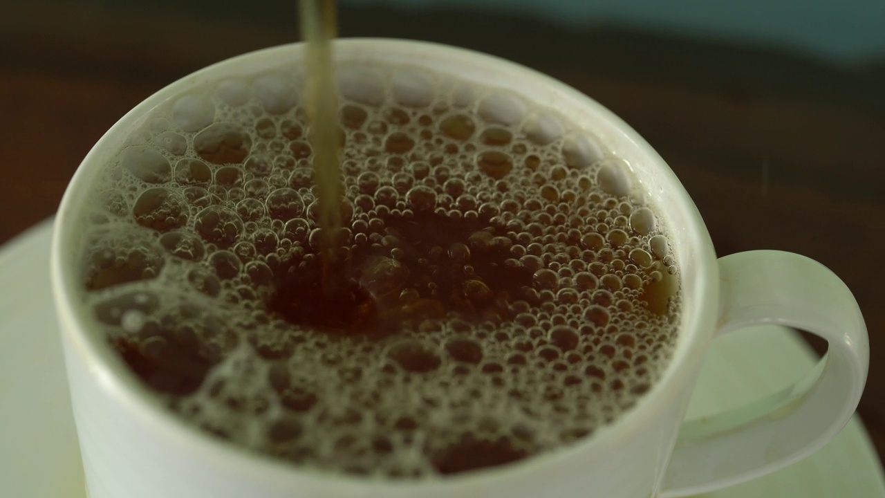 将茶从透明玻璃茶壶中倒入陶瓷茶杯中。健康饮料的概念。视频素材