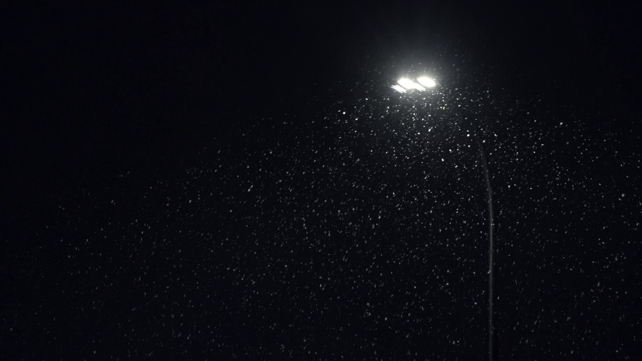 冬天的夜晚，城市街道上用现代街灯背光飘落的雪花。公园里的雪花被明亮的灯光照亮。降雪、暴风雪和强风视频素材