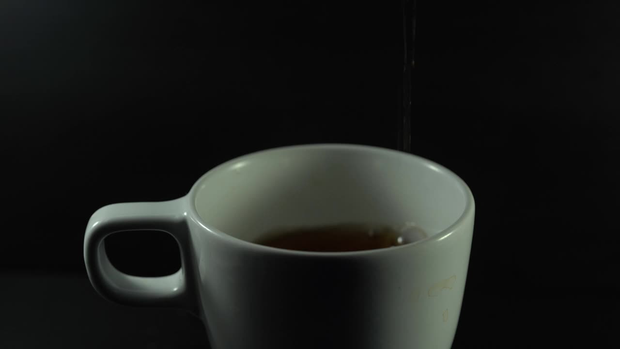 将茶从透明玻璃茶壶中倒入陶瓷茶杯中。视频素材