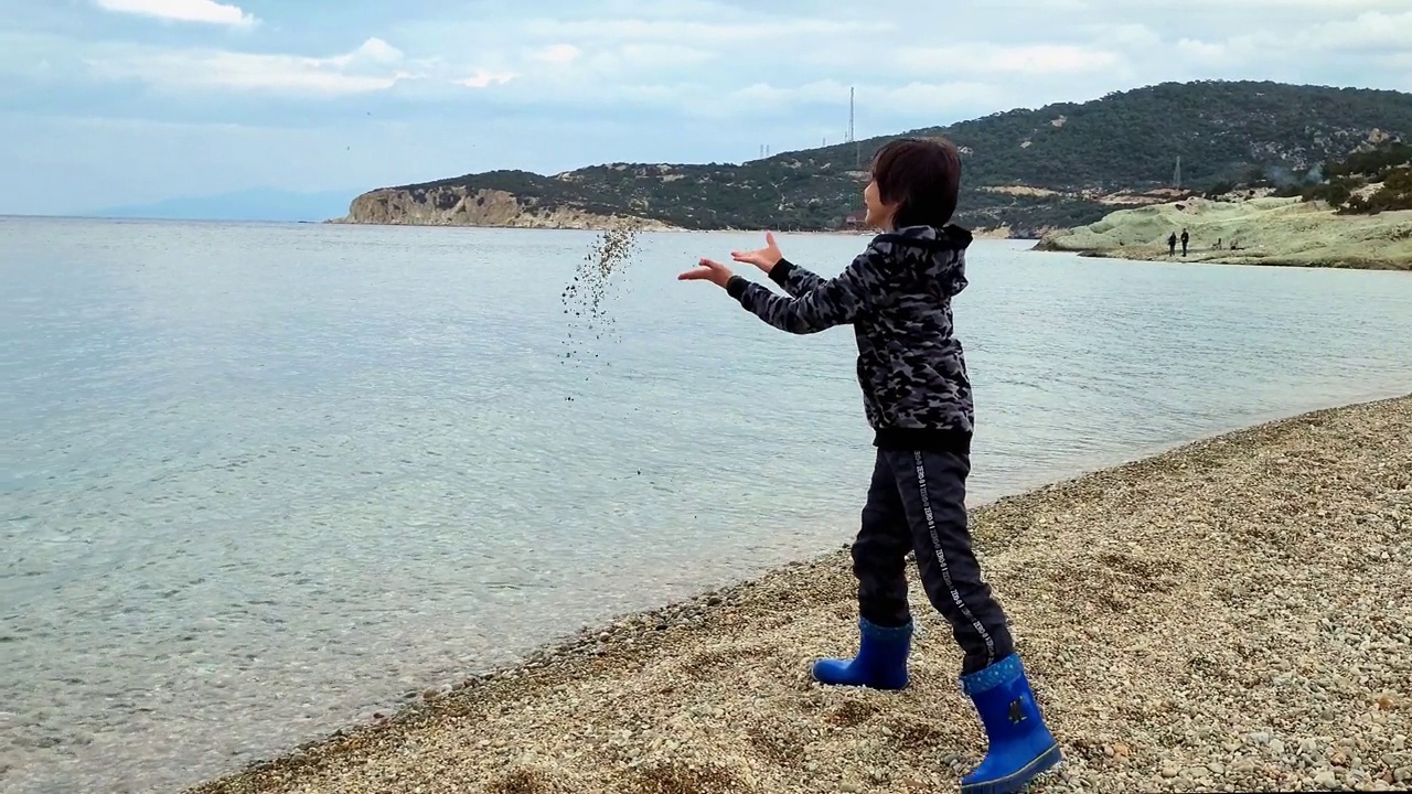 快乐的男孩在海滩上向大海扔石头视频素材