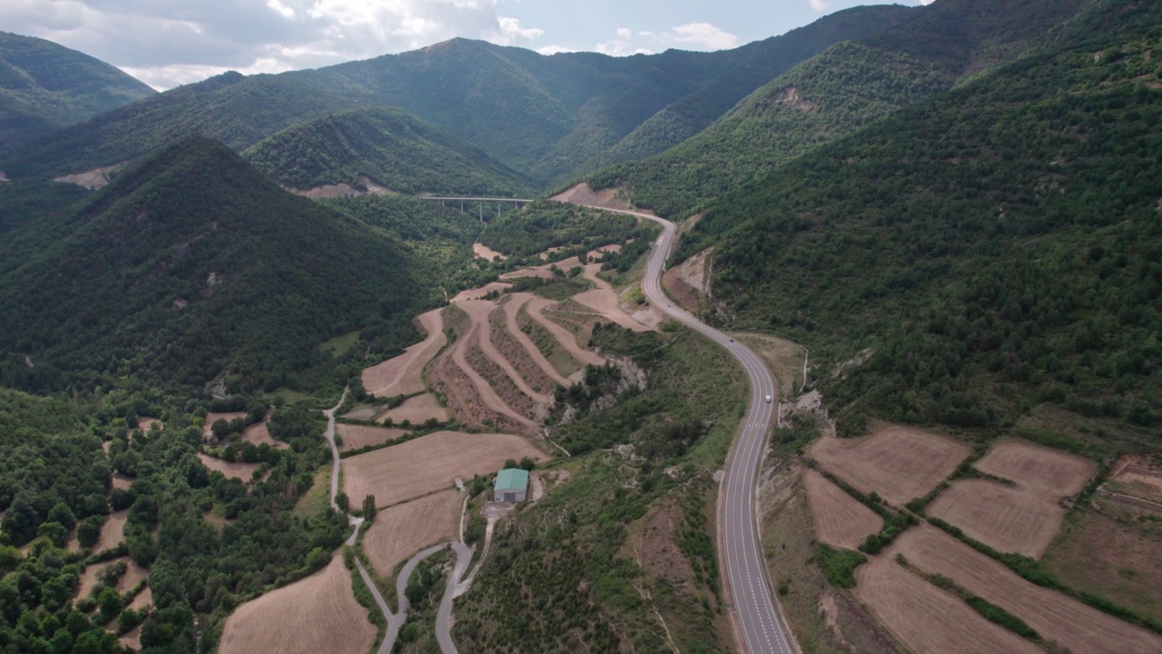 美丽的无人机视图沥青道路在高山上。山脉消失在天空中，天空略有多云，但山峰被太阳照亮。视频素材