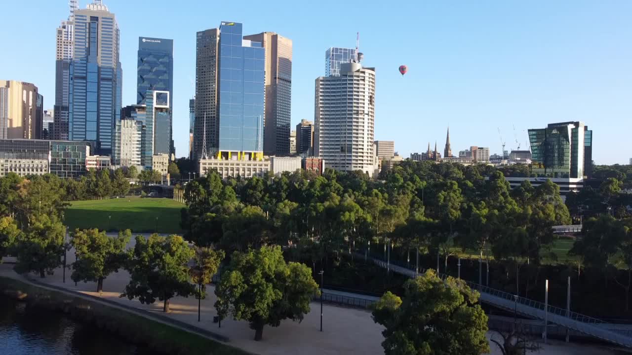 在澳大利亚维多利亚州的Birrarung Marr，热气球飞过墨尔本中央商务区。拂晓时对城市的无人机航拍。视频素材