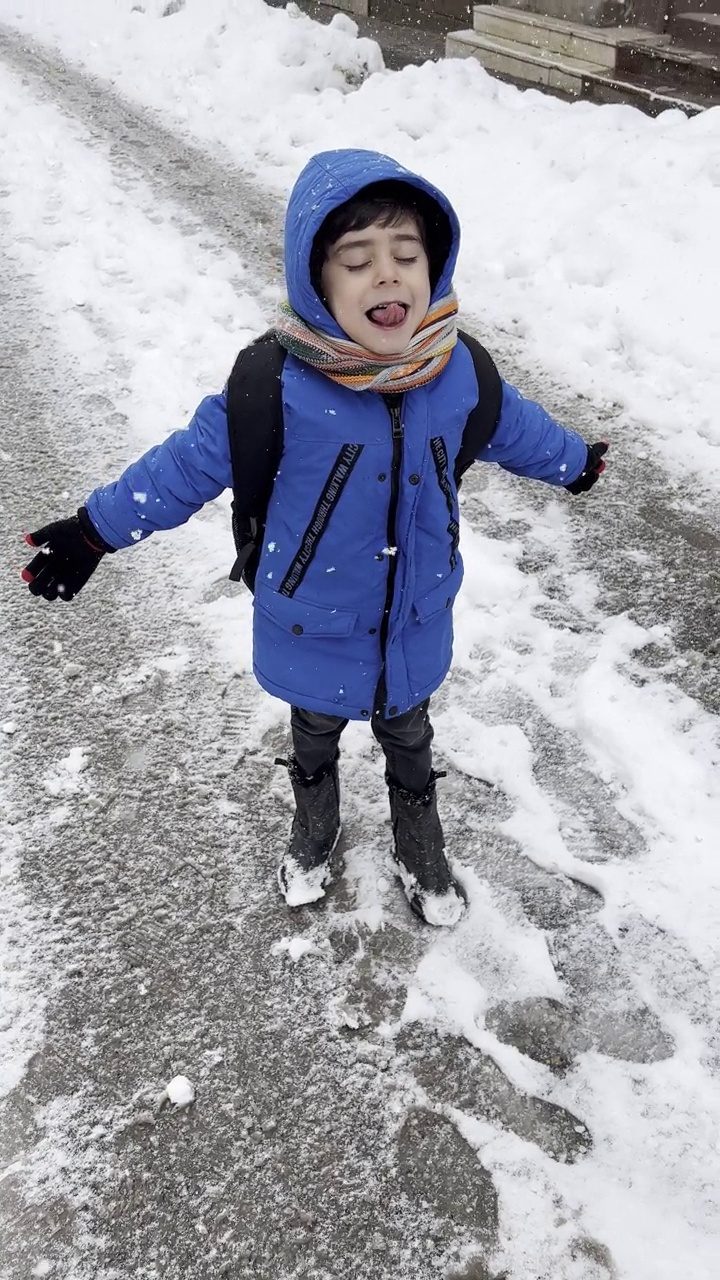 穿着蓝色冬衣的滑稽小男孩在下雪时行走。儿童冬季户外活动。视频素材