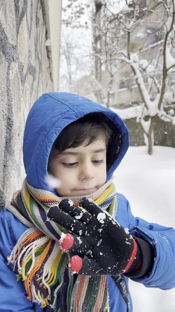 穿着蓝色冬衣的滑稽小男孩在下雪时行走。儿童冬季户外活动。视频素材