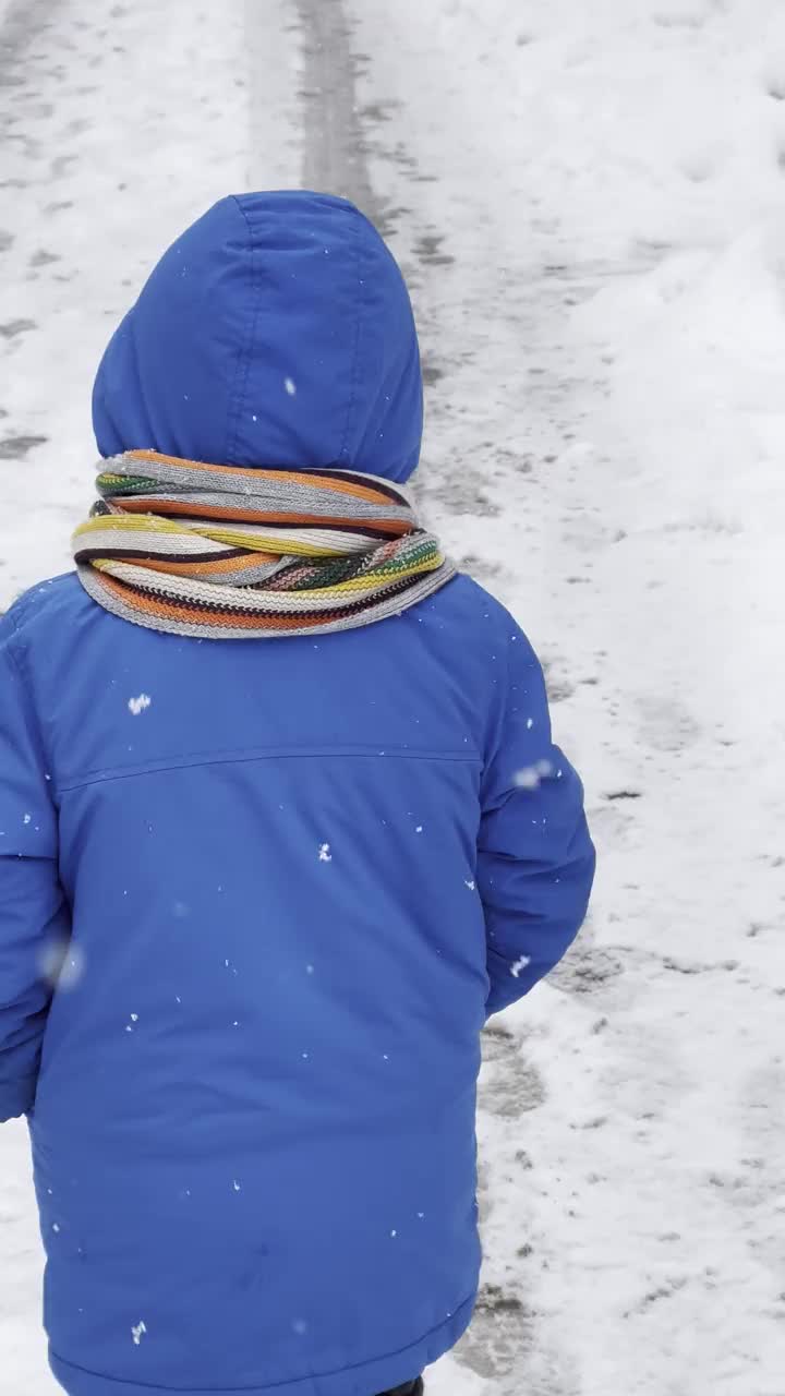 穿着蓝色冬衣的滑稽小男孩在下雪时行走。儿童冬季户外活动。视频素材