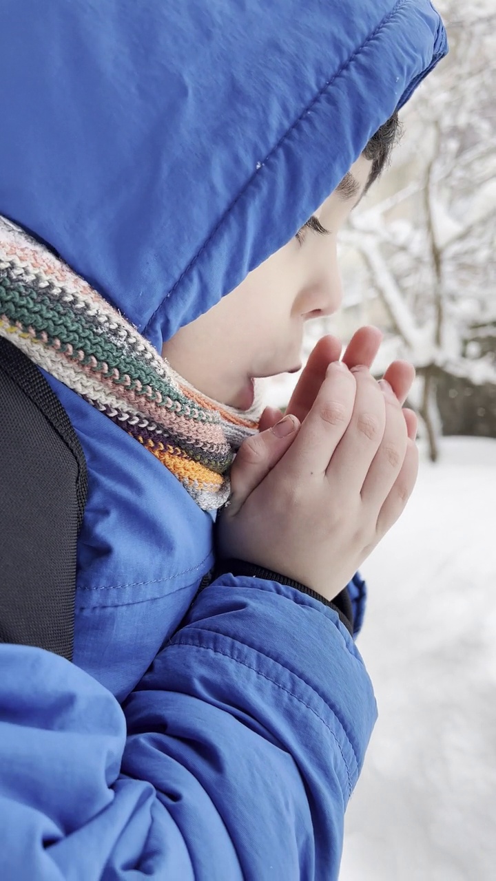 穿着蓝色冬衣的滑稽小男孩在下雪时行走。儿童冬季户外活动。视频素材