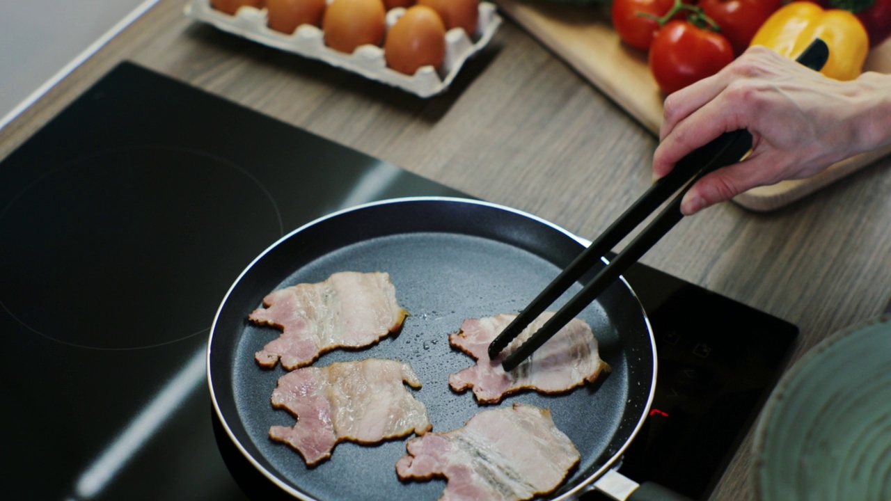 女人准备培根做早餐。早餐煎培根。用平底锅把咸肉片煎一下。前视图。视频素材