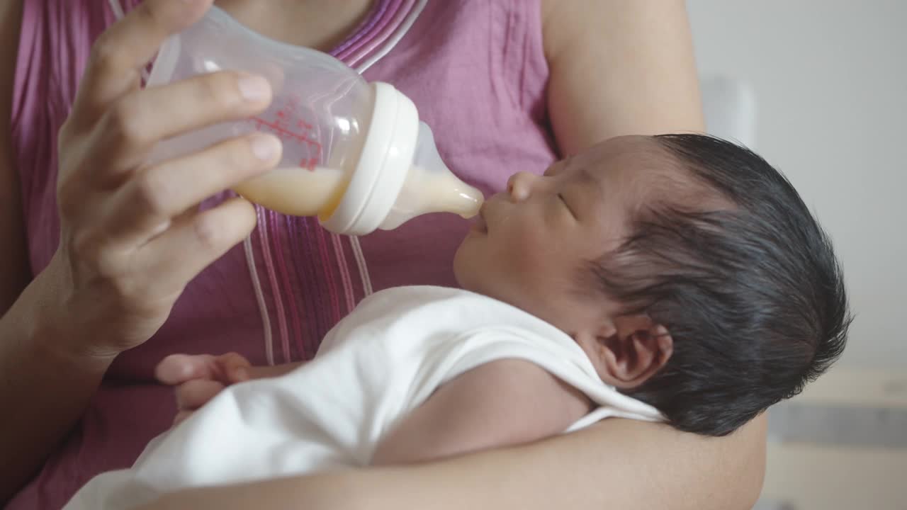 亚洲母亲用奶瓶喂她的新生婴儿在她的怀里。视频素材