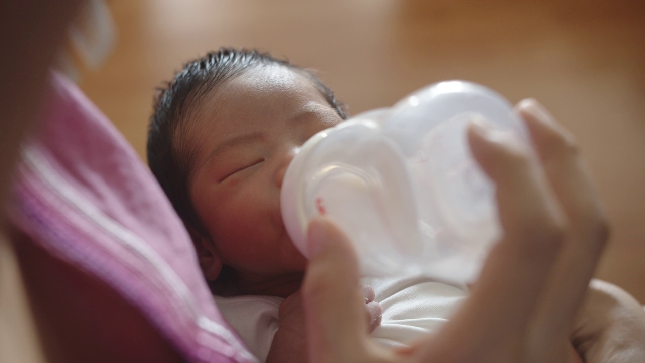 亚洲母亲用奶瓶喂她的新生婴儿在她的怀里。视频素材