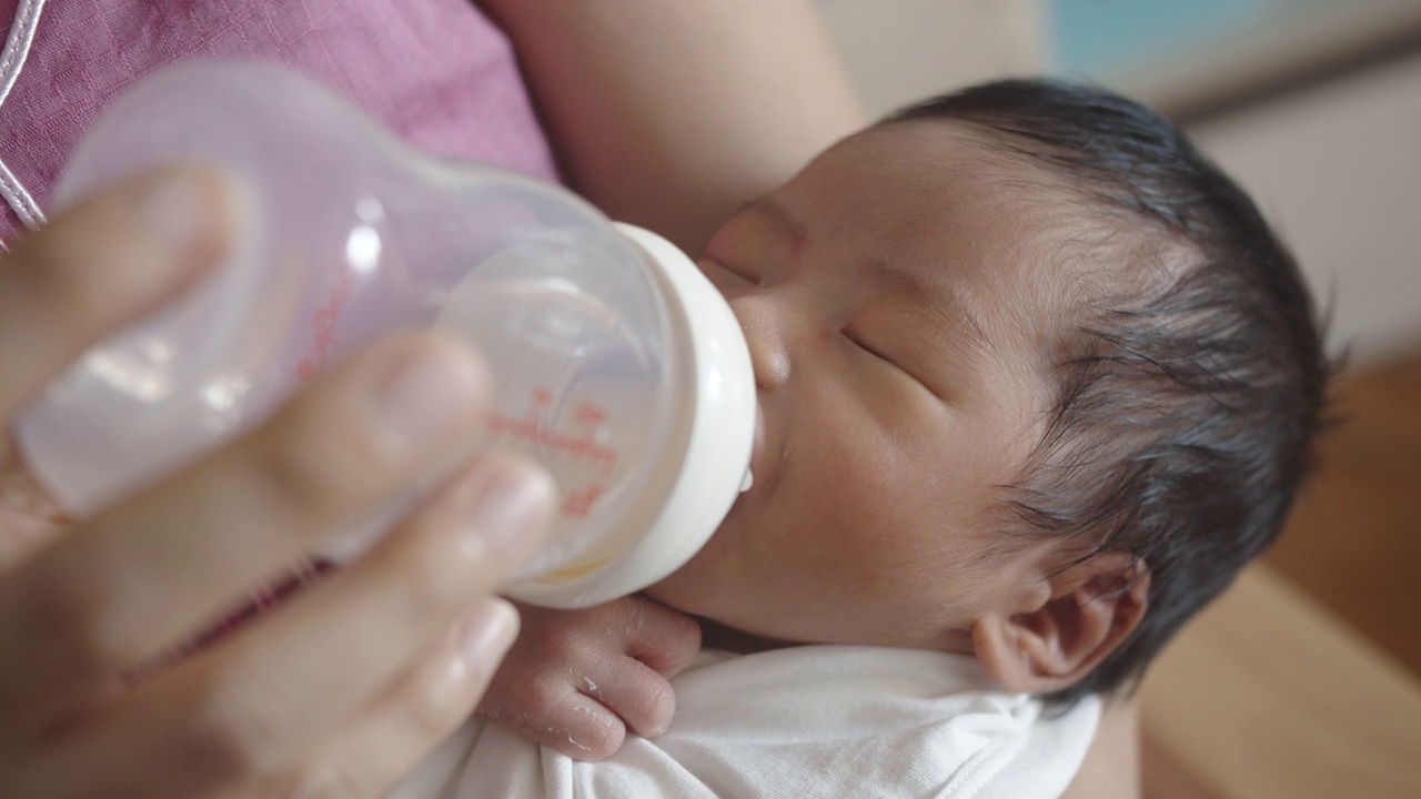 亚洲母亲用奶瓶喂她的新生婴儿在她的怀里。视频素材