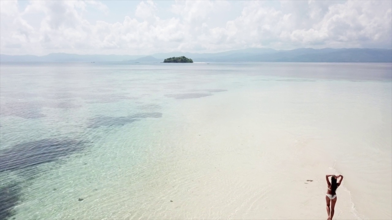 年轻的比基尼女子走在白色沙滩附近的蓝色热带海洋海浪。视频素材