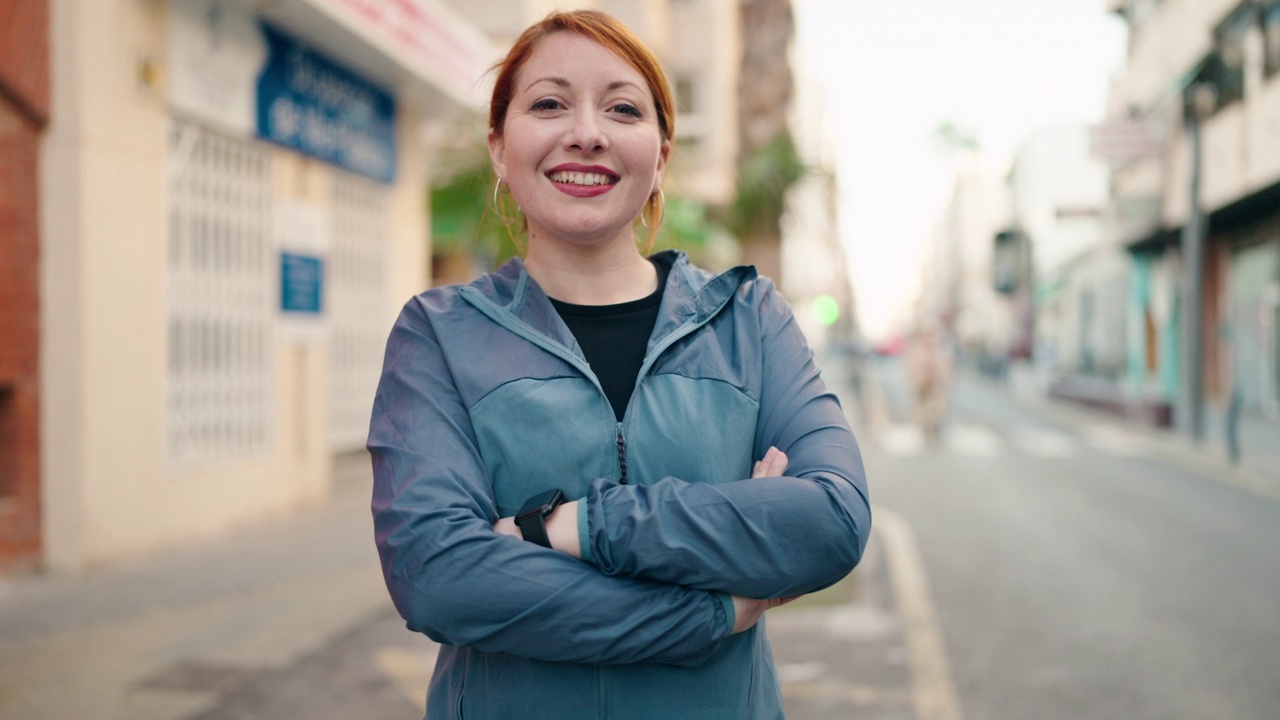 身穿运动服的年轻红发女子双臂交叉站在街上视频素材