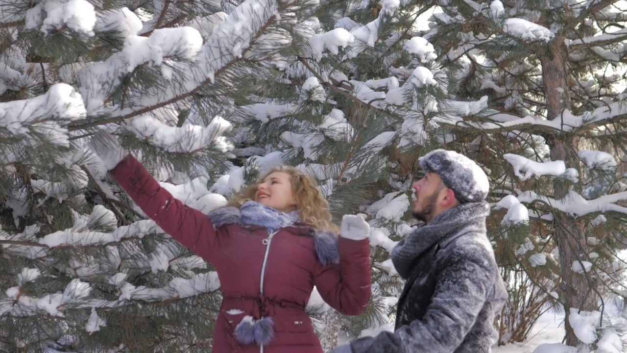 缓慢的运动。一个漂亮的年轻人和一个女孩把雪抛向空中。寒冷的冬天，一对浪漫的夫妇在一个下雪的城市公园里享受美好的时光。恋人之间温柔的关系视频素材