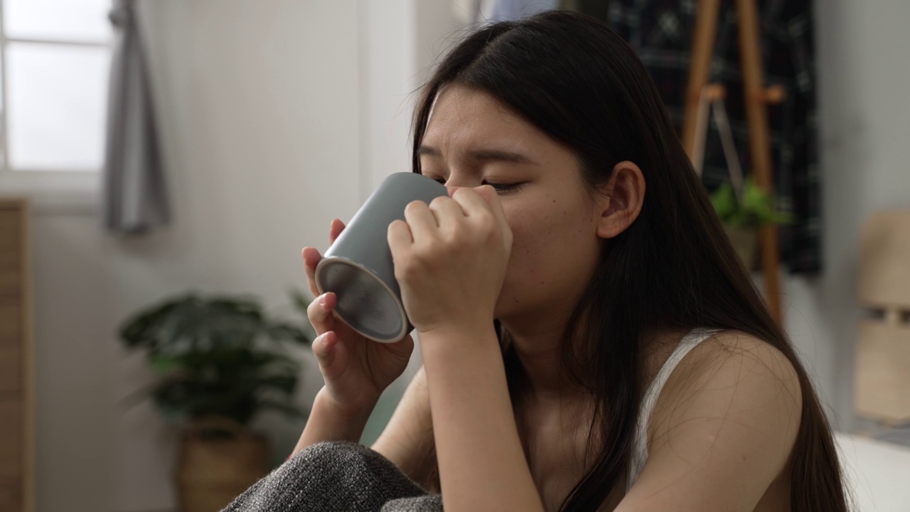 一个快乐的亚洲女性的头部照片，在家里的卧室里度过一个平静的早晨后，她在床上喝了美味的咖啡，感觉神清气爽。视频素材