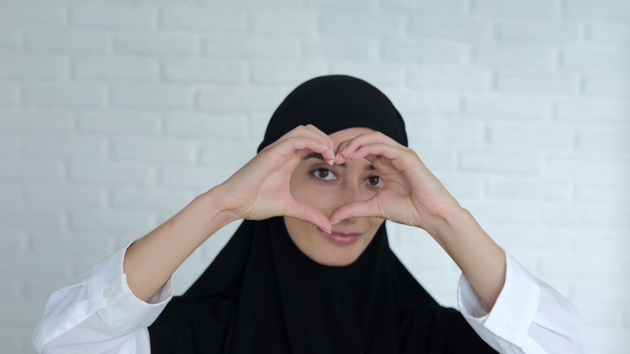 一名穆斯林妇女戴着黑色的希贾布微笑，并用手指交叉成心形表示爱。象征着伊斯兰世界对全世界的爱视频素材