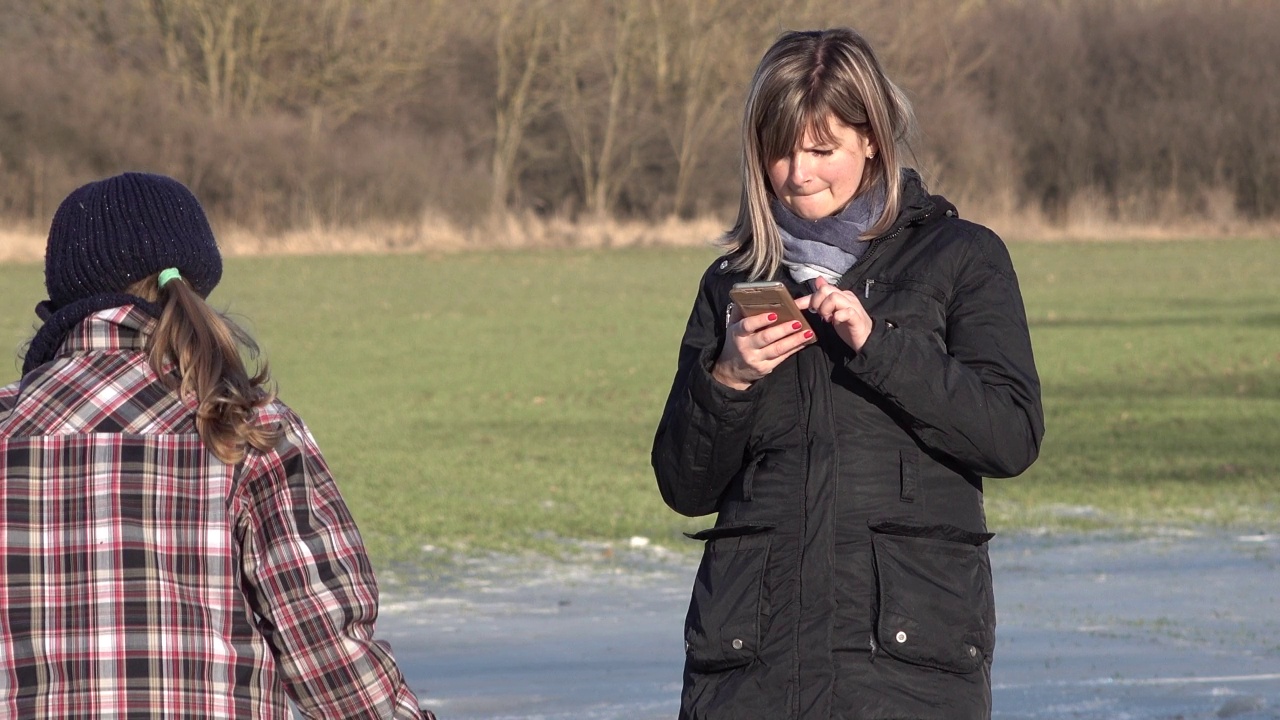 年轻的母亲在冰上，使用智能手机上的应用程序视频下载