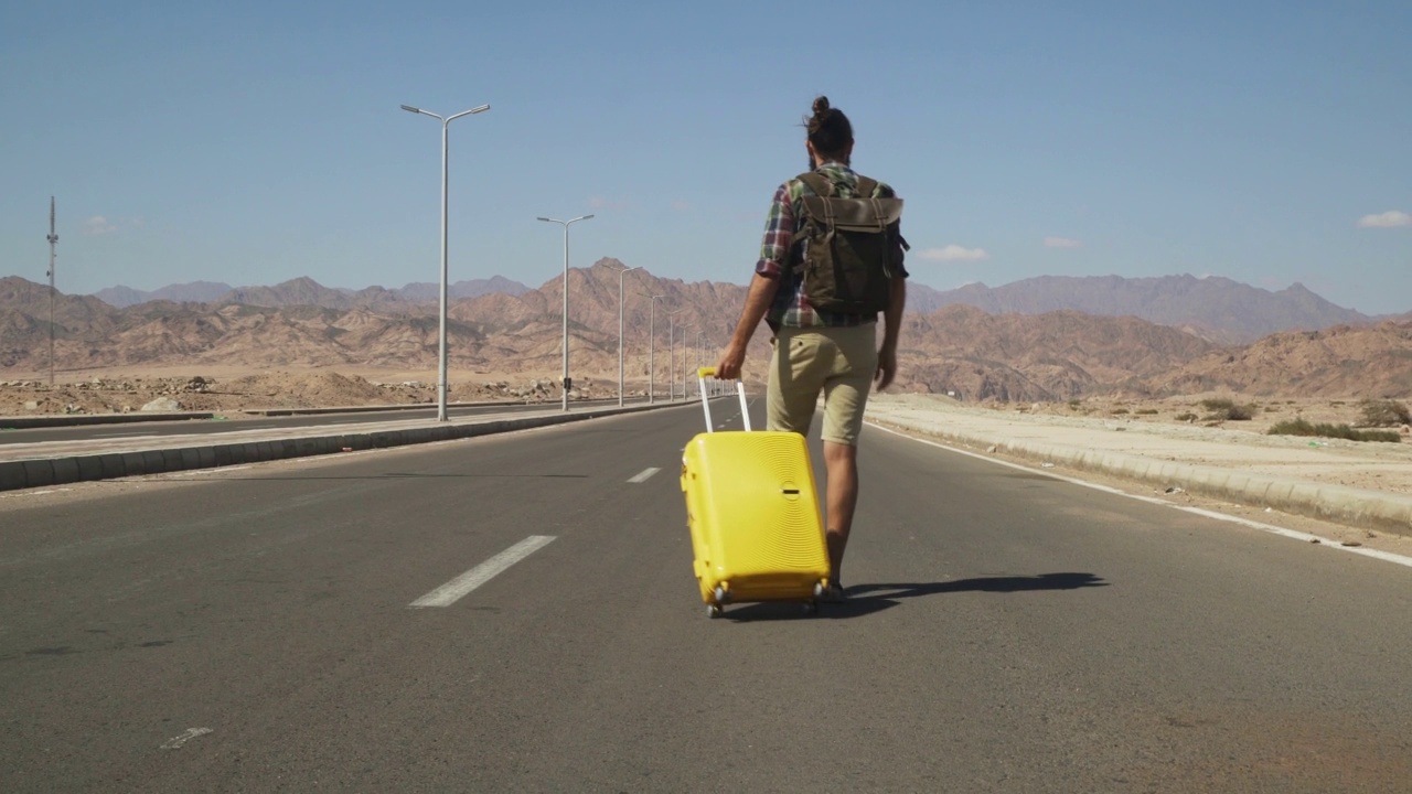 年轻的男性旅行者带着黄色的行李和背包走在高速公路上视频素材