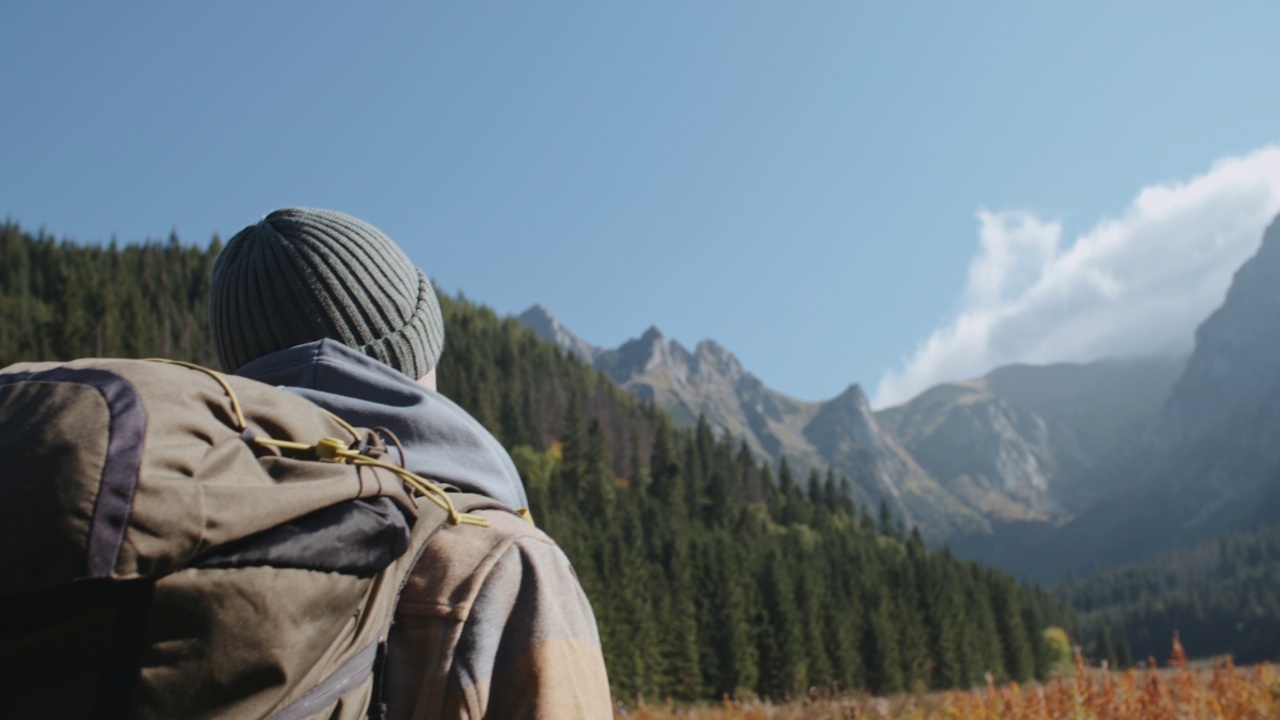 特写手持跟随男性徒步旅行者走在山谷的小道上背包，美丽的山峰和森林的背景。男子背包客在波兰高地徒步旅行。探险旅行探险视频素材