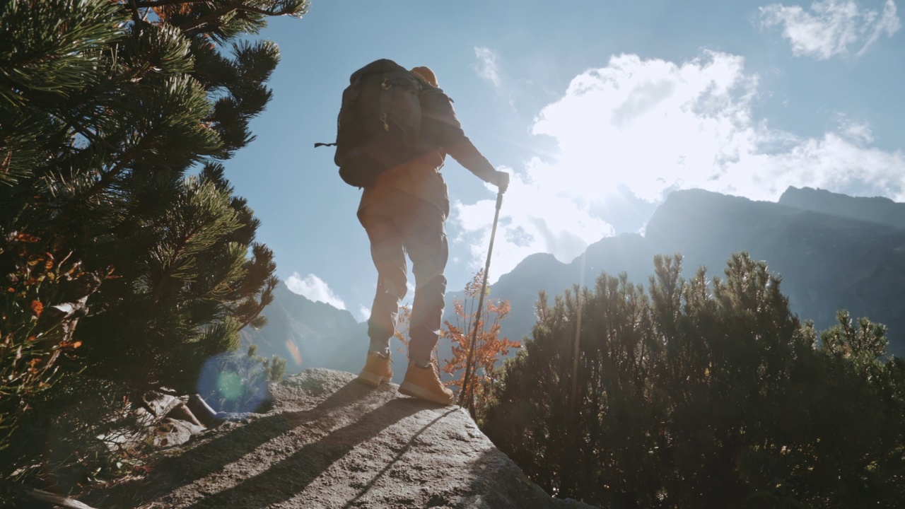 男性徒步旅行者带着登山杖到达可以俯瞰美丽山脉的地点。男子旅行者站在岩石上看令人难以置信的高地景观在阳光明媚的一天。山峰视频素材