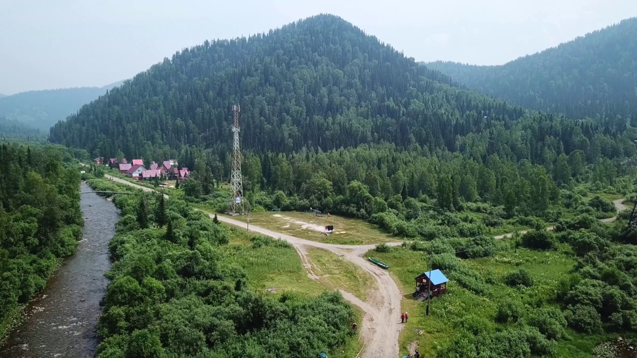 无人机在山区乡村的河流上空飞行。鸟瞰雄伟的山峦，针叶林风光。视频素材