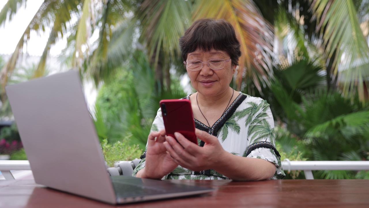 老年女性在户外使用笔记本电脑和手机视频素材