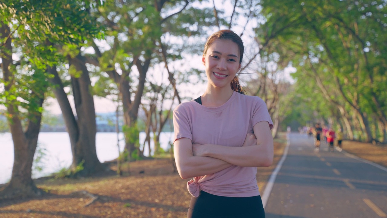 亚洲积极运动的女性在户外运动后站在自信。美丽的女孩的肖像在运动服微笑，交叉手臂和看着相机后，在晚上在公园跑步锻炼。视频素材