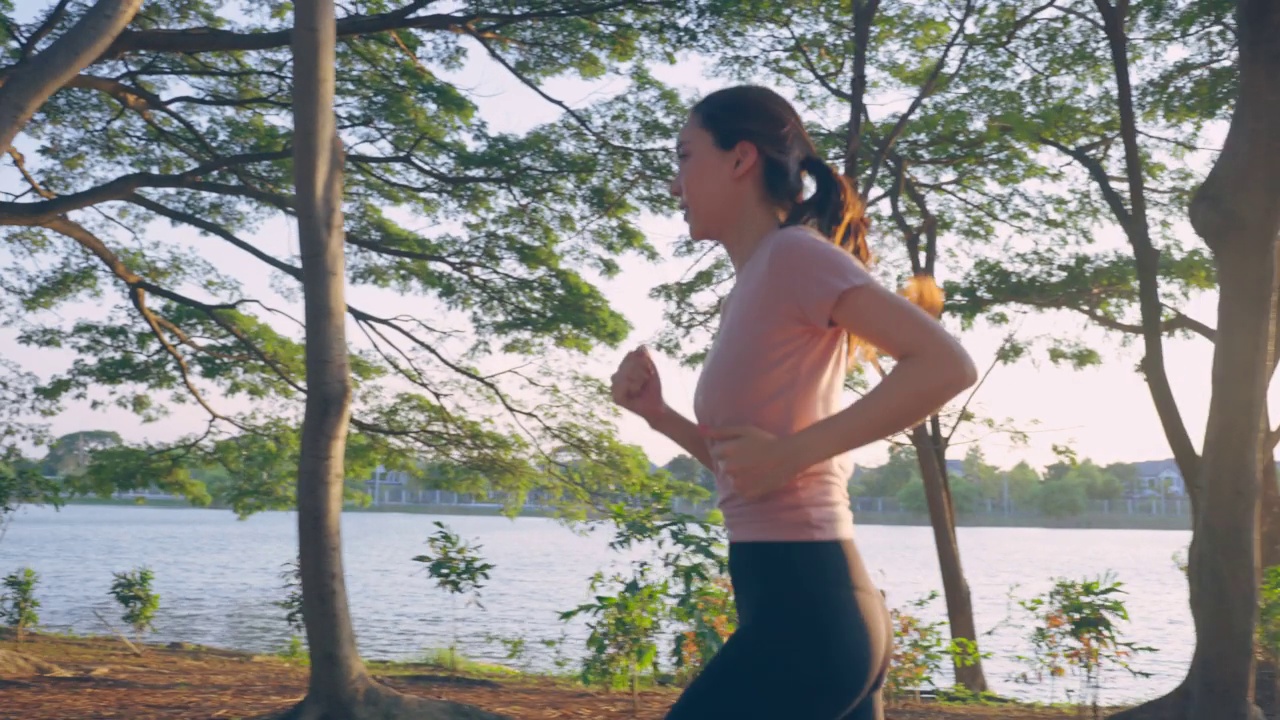 亚洲年轻美丽的运动女子在公园的街道上跑步。美丽的运动员和坚定的女孩在运动服装锻炼慢跑锻炼户外保健在傍晚日落在花园。视频素材