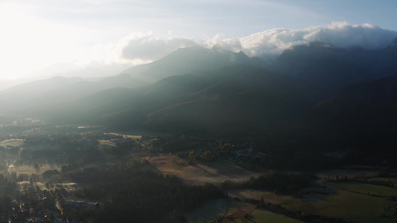 在明亮的阳光照耀下的高山村的秋日清晨，空中有雾。无人机拍摄的史诗般的山峰覆盖着起伏的云朵在日出的光线。令人难以置信的风景，美丽的山谷视频素材