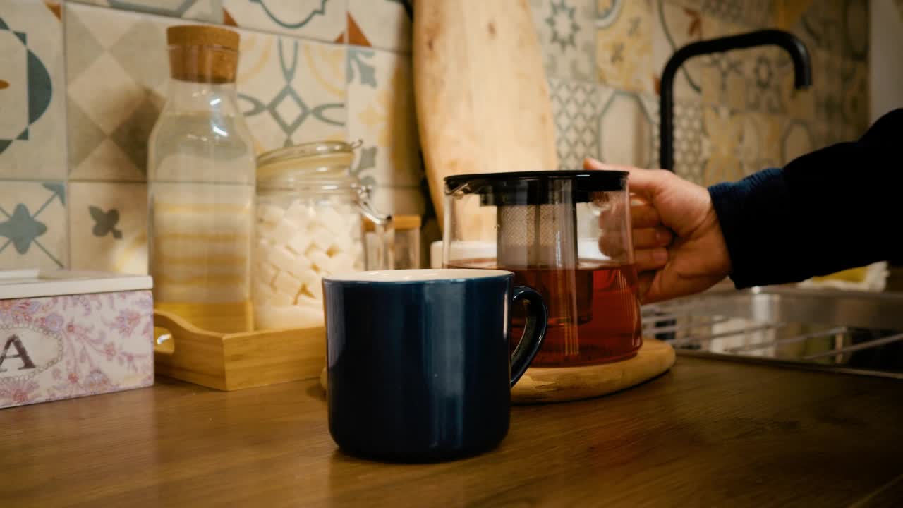 一个男人的手把刚泡好的茶倒进杯子里。阳光明媚的早晨视频下载