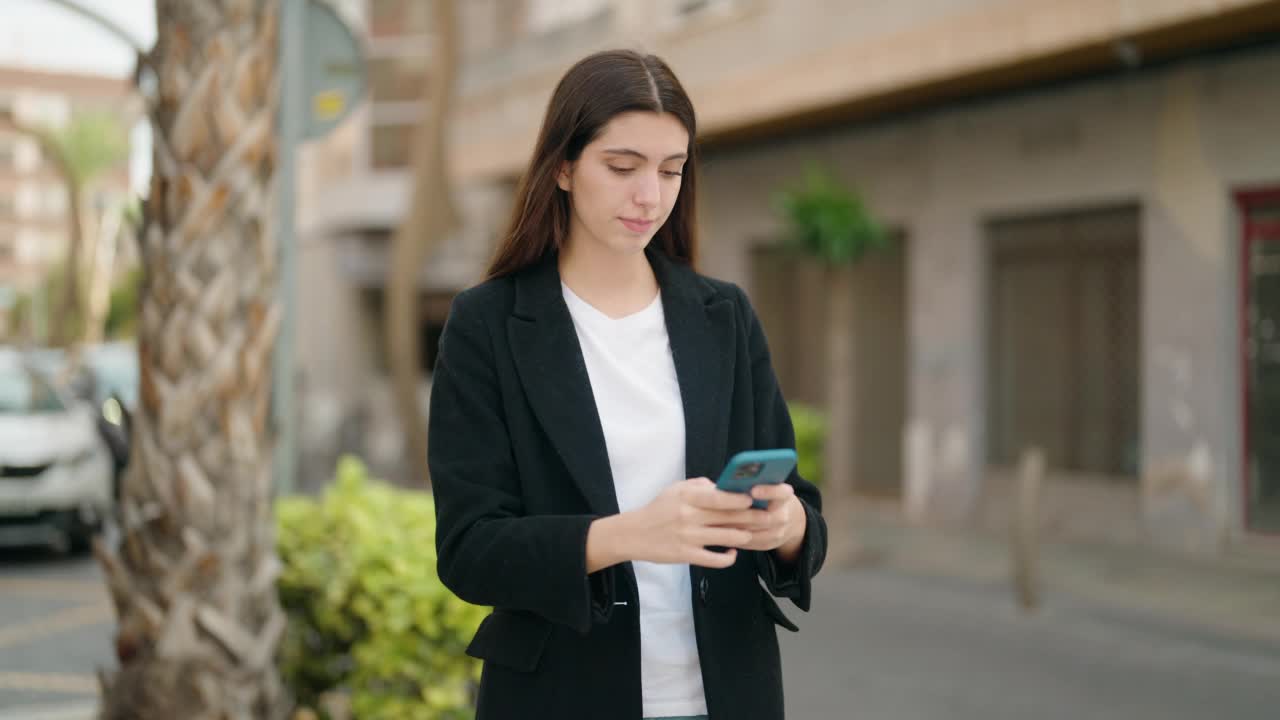 年轻的西班牙女孩微笑自信地在街上用智能手机自拍视频素材