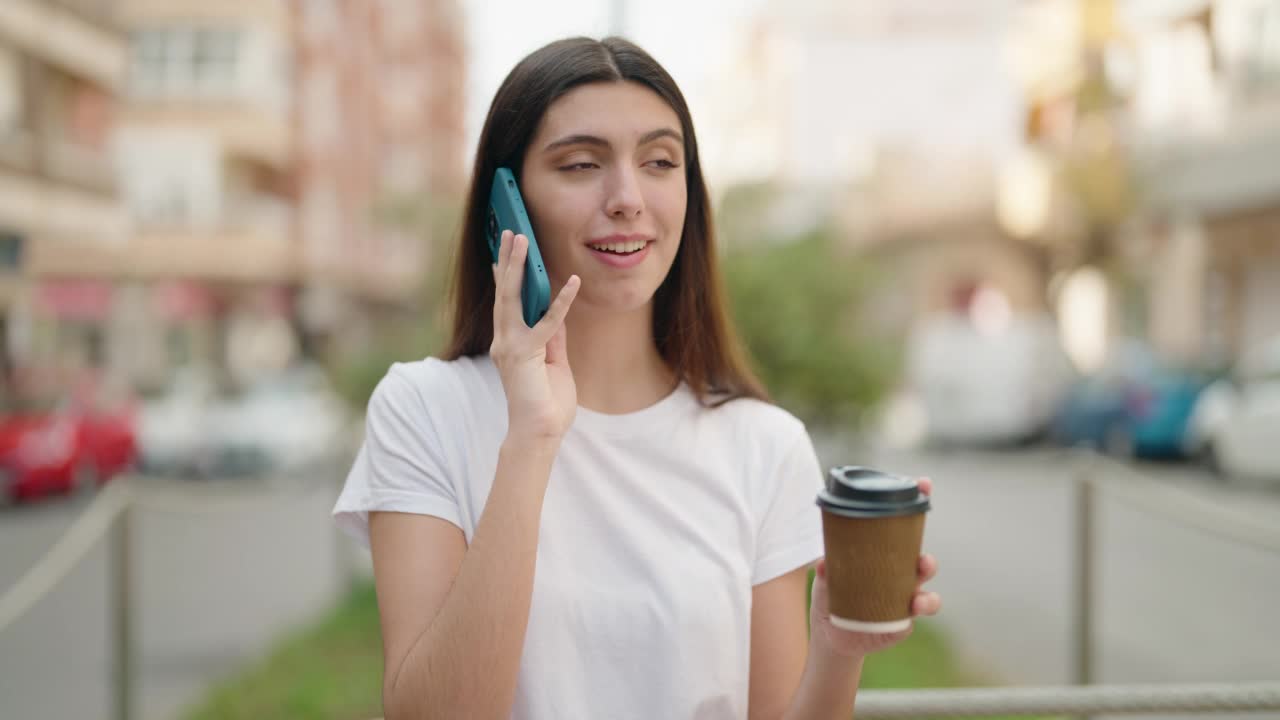 年轻的西班牙女孩在街上喝咖啡，用智能手机聊天视频素材