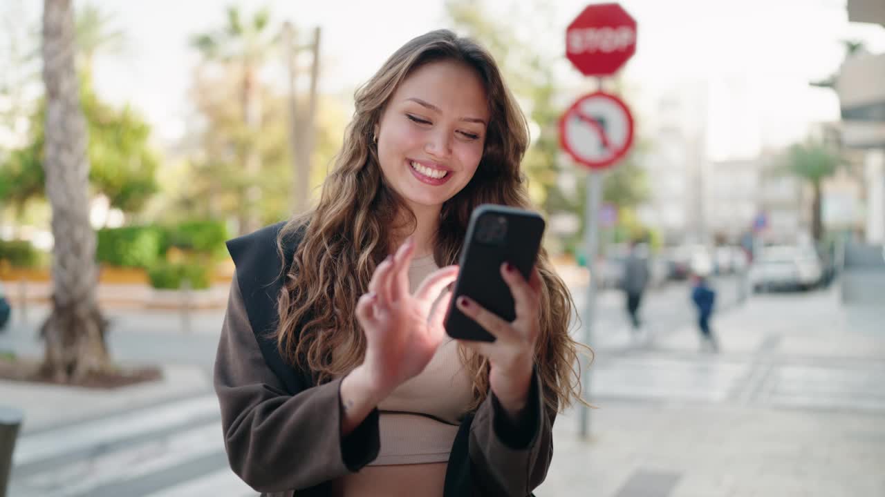 年轻的西班牙女性微笑着自信地在街上使用智能手机视频素材