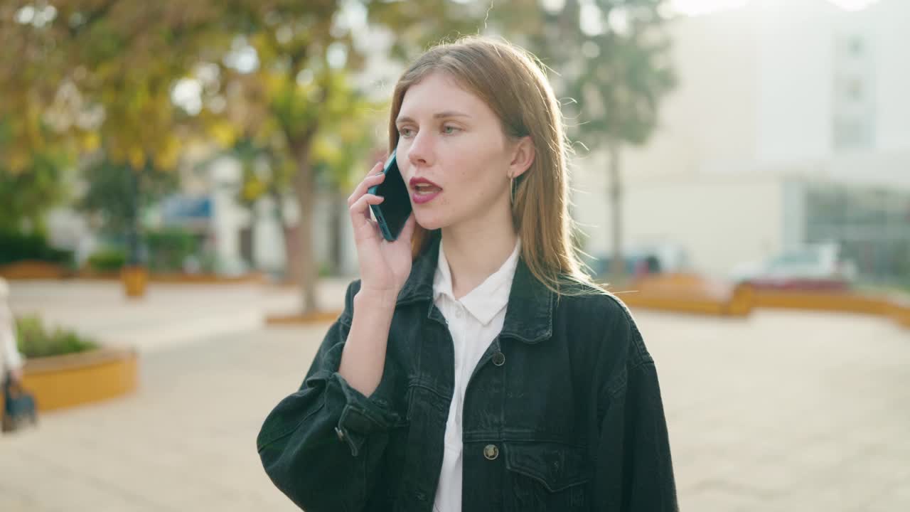 年轻的白人女性在公园看手表，在智能手机上说话视频素材