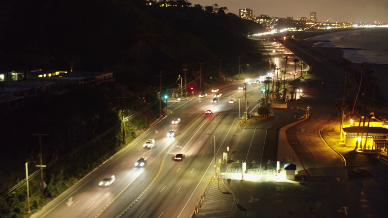 在加利福尼亚的圣莫尼卡，灯火通明的汽车在夜间沿着海滩的道路行驶视频素材