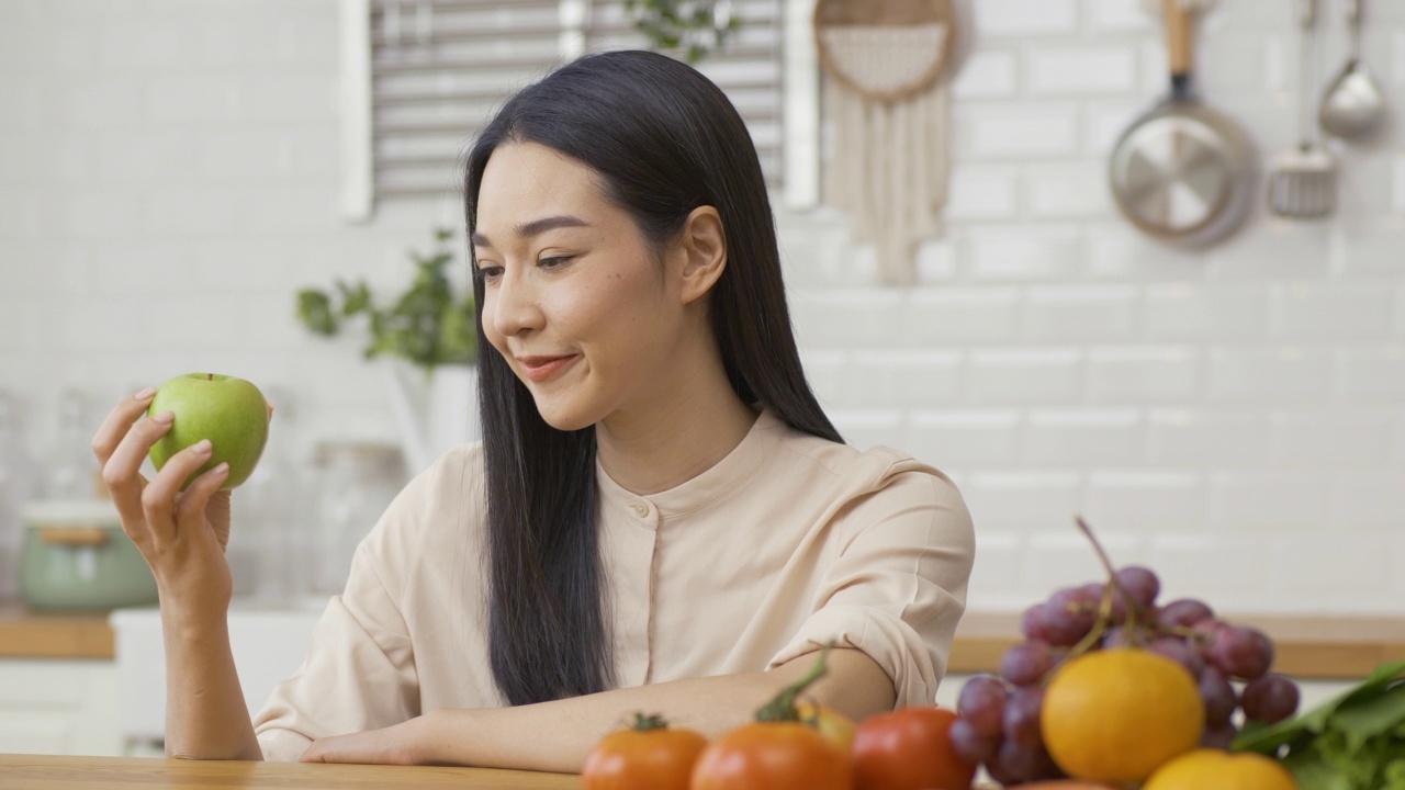 美丽的亚洲女人手里拿着橘子在厨房。她看着镜头，微笑着。视频素材