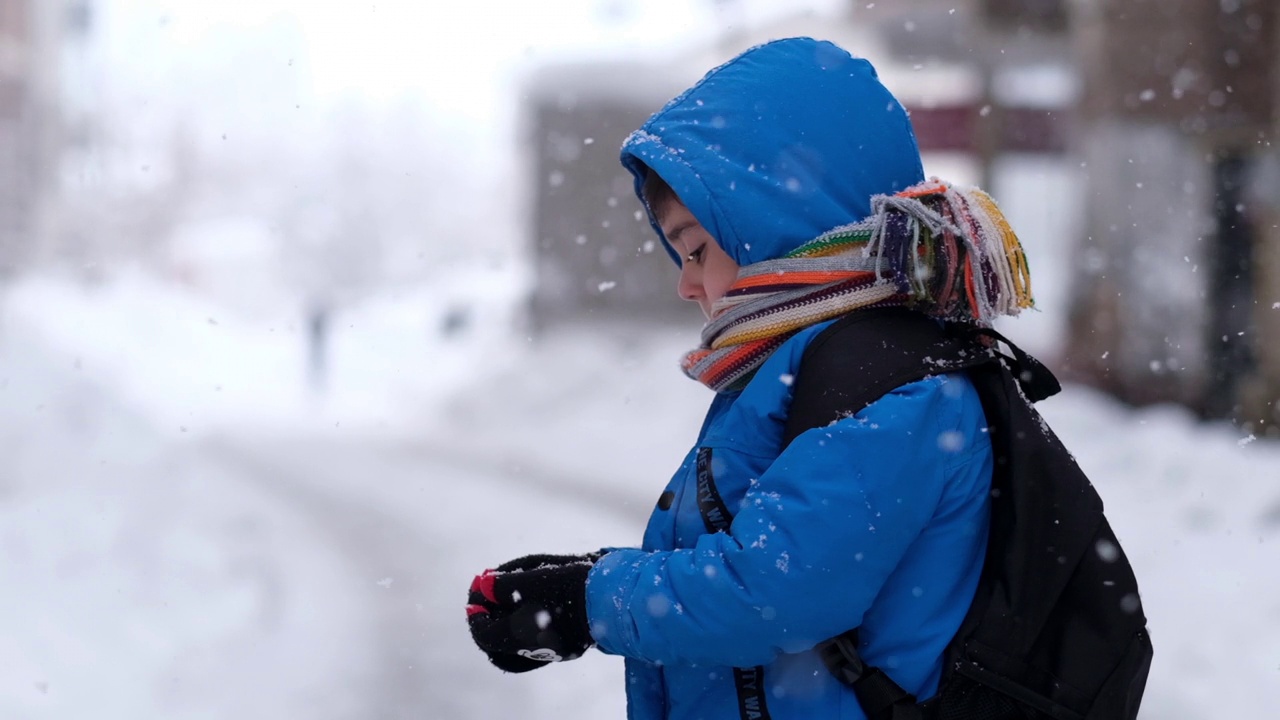 穿着蓝色冬衣的滑稽小男孩在下雪时行走。儿童冬季户外活动视频素材