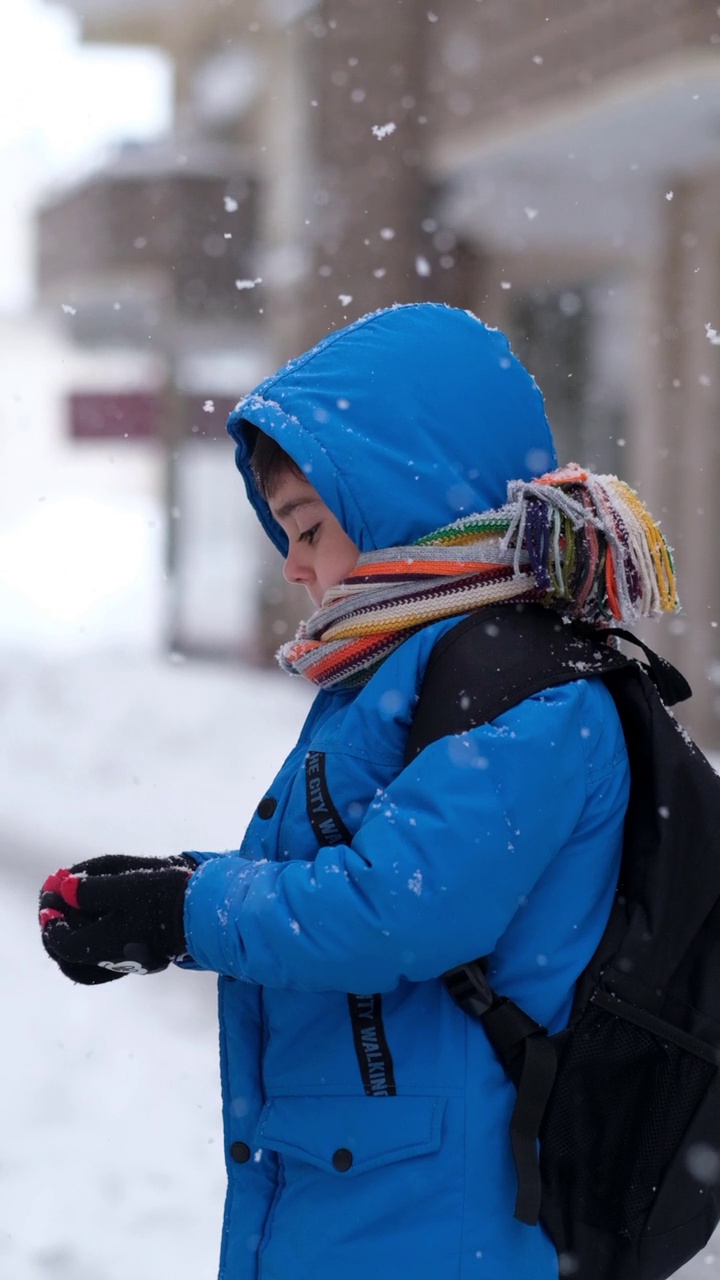 穿着蓝色冬衣的滑稽小男孩在下雪时行走。儿童冬季户外活动视频素材