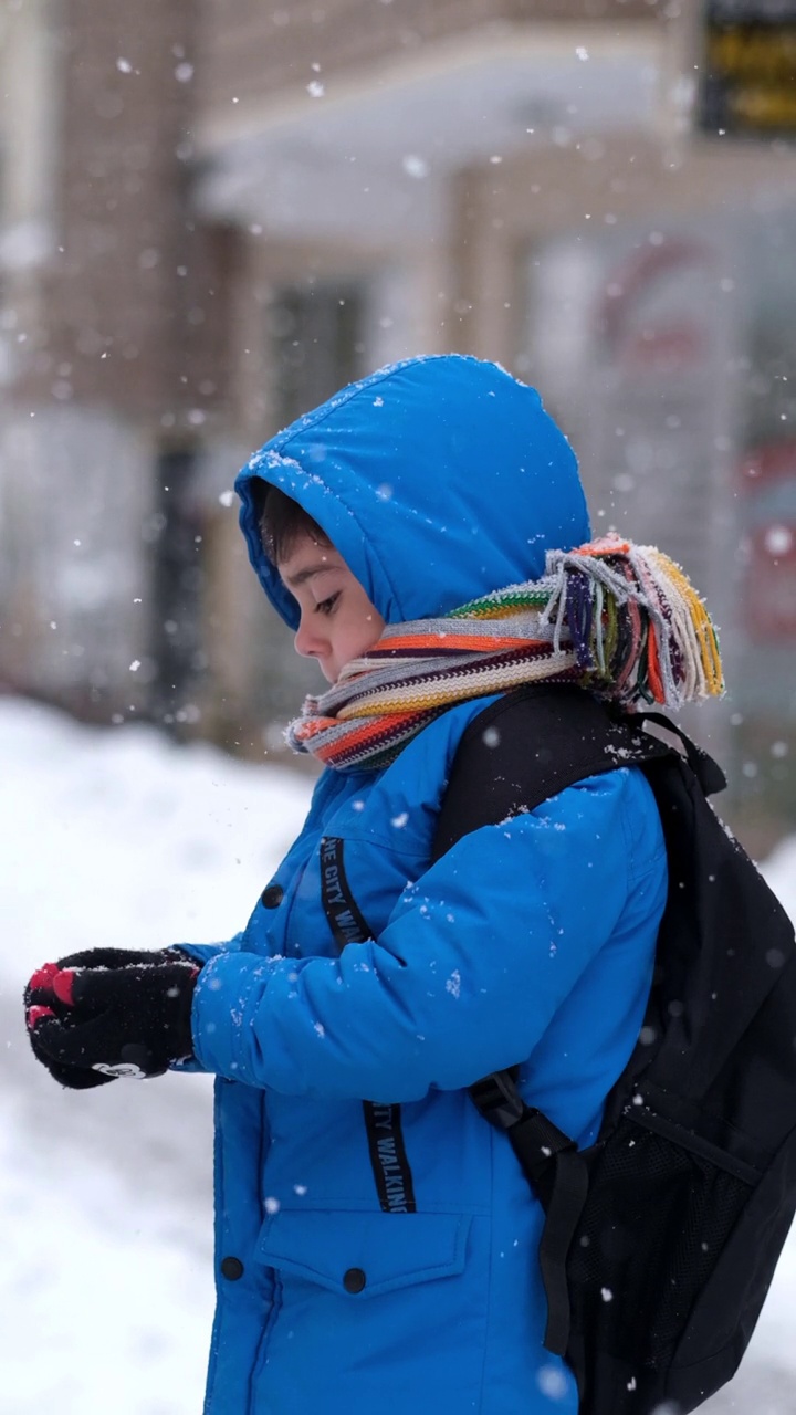 穿着蓝色冬衣的滑稽小男孩在下雪时行走。儿童冬季户外活动视频素材