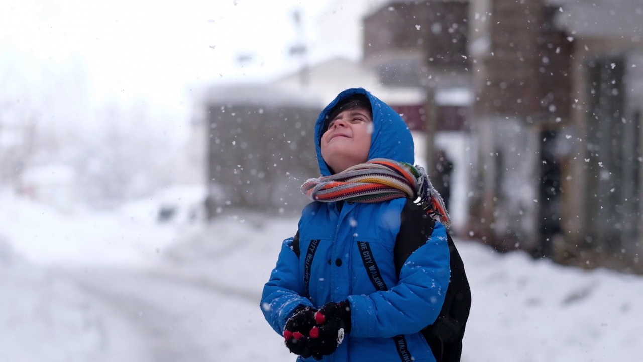 穿着蓝色冬衣的滑稽小男孩在下雪时行走。儿童冬季户外活动视频素材