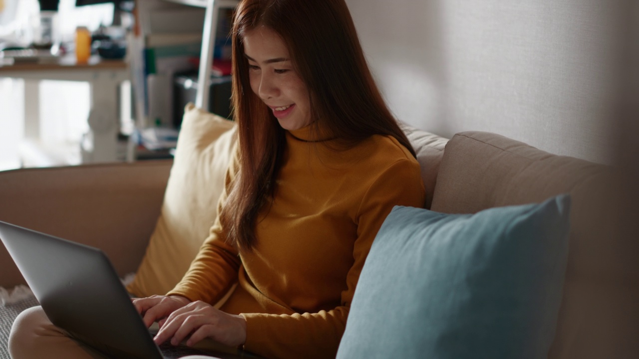 快乐的年轻女人在家里用笔记本电脑视频素材