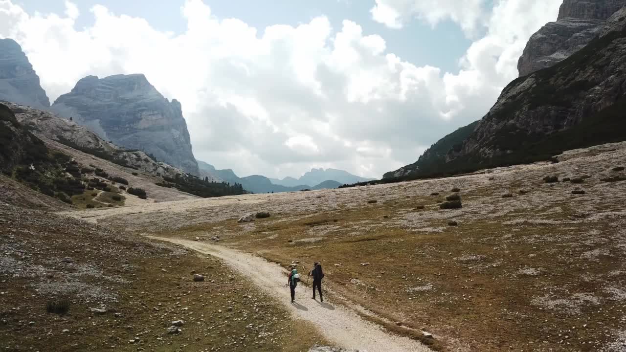 一对夫妇沿着一条穿过意大利白云石山谷的砾石小路徒步旅行。四周是高耸的山峰。石头和原始的景观。偏僻荒凉的地方自由的探索视频素材