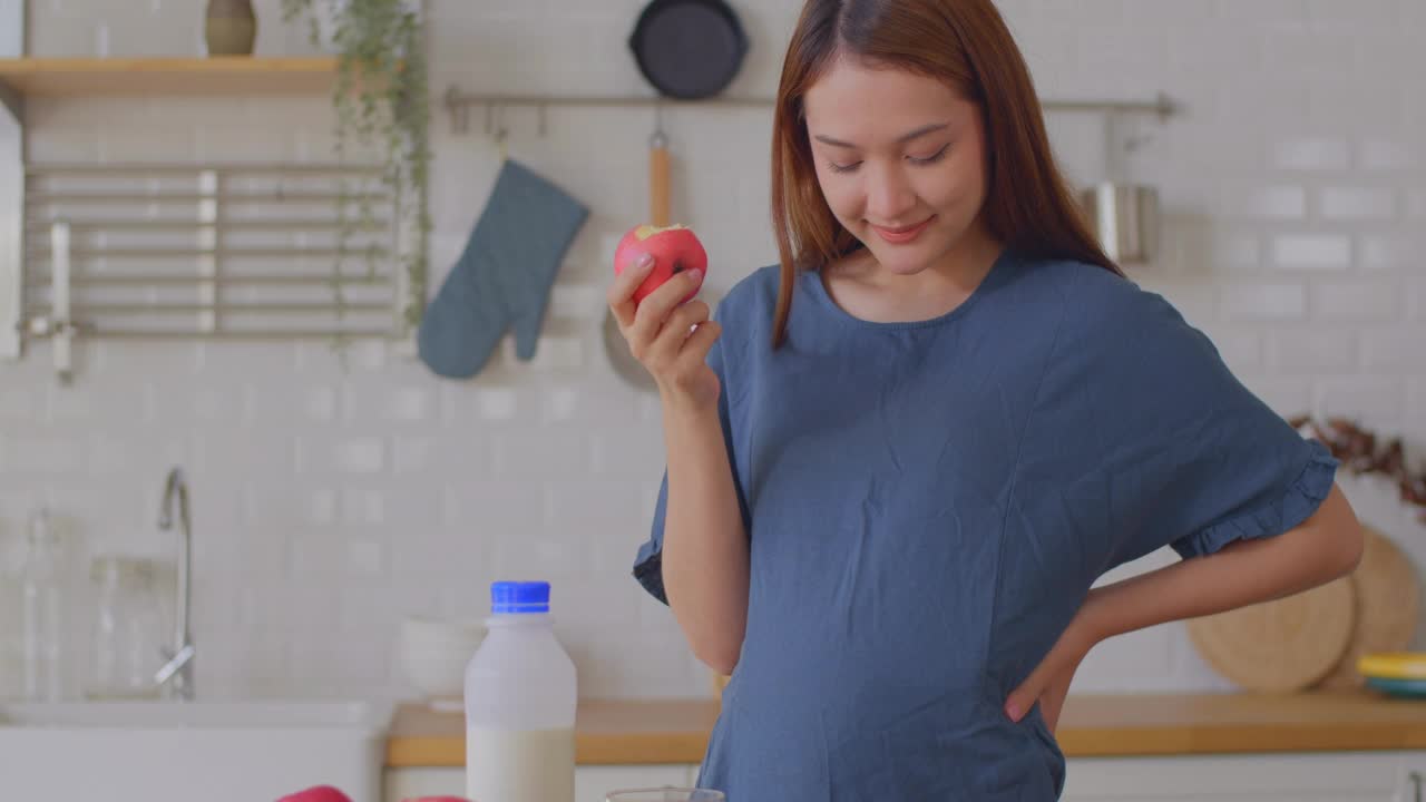 一个孕妇喝着牛奶，吃着苹果，轻轻地摸着肚子，怀孕/分娩视频素材